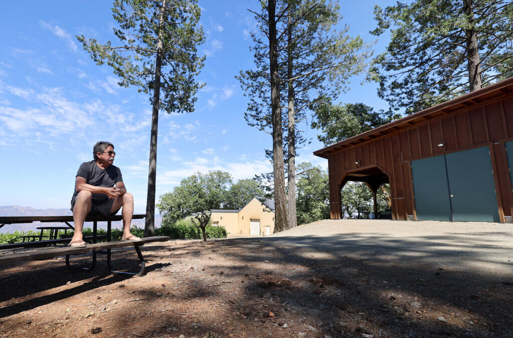 Sheldon Richards, owner of Paloma Vineyard, sits on a picnic table in Napa County whereas a portion of his winery building and garage in located in Sonoma County. Photo taken at Paloma Vineyard near St. Helena, Tuesday August 1, 2023. (Beth Schlanker / Press Democrat)